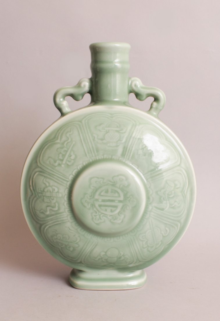 A CHINESE CELADON PORCELAIN MOON FLASK, each domed: A CHINESE CELADON PORCELAIN MOON FLASK, each domed surface centred by a raised Shou symbol encircled by ribboned Buddhist emblems, the base with a Qianlong seal mark, 13.7in high.