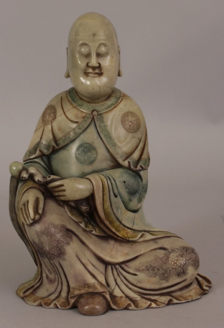A CHINESE STAINED SOAPSTONE FIGURE OF A SEATED LOHAN,: A CHINESE STAINED SOAPSTONE FIGURE OF A SEATED LOHAN, with one knee raised and holding a fly whisk, 6.1in wide at widest point & 8.6in high.