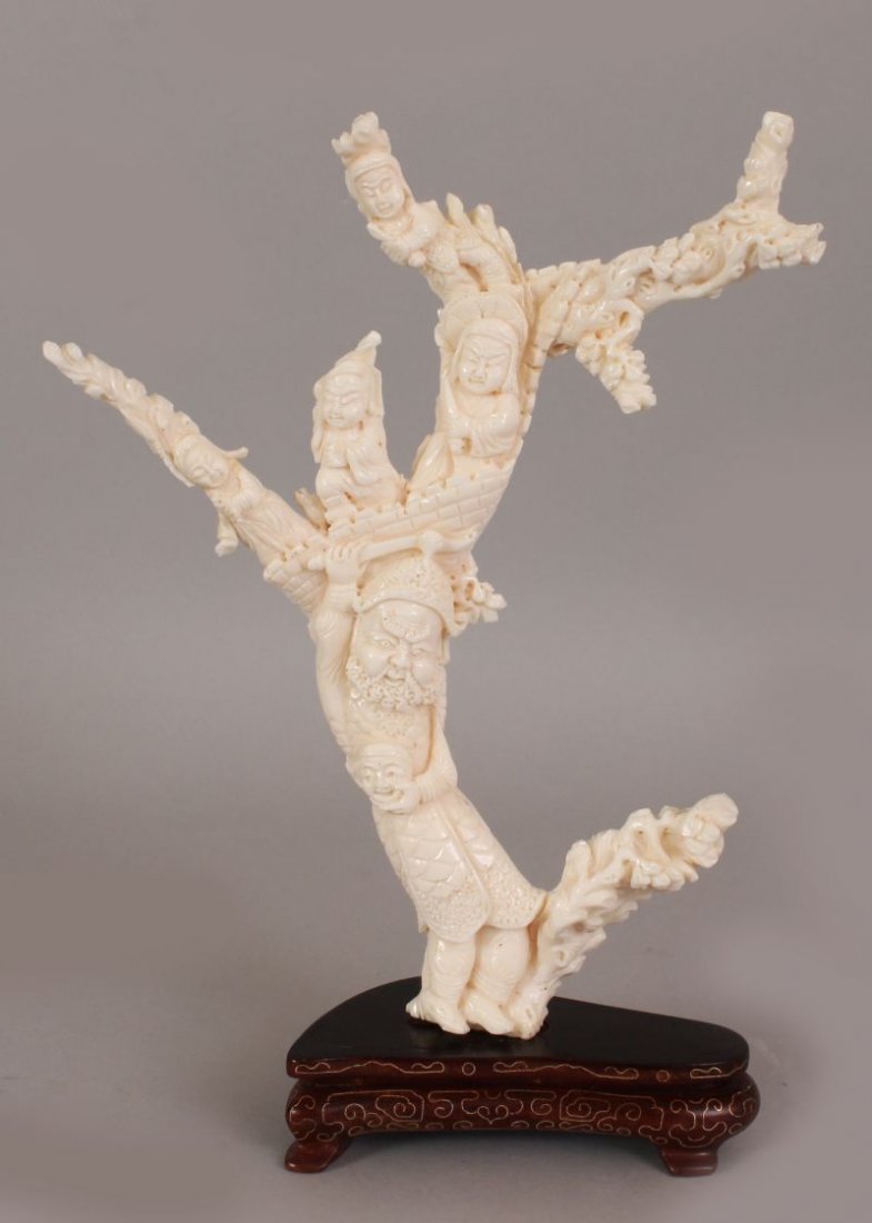 A GOOD EARLY 20TH CENTURY CHINESE WHITE CORAL CARVING,: A GOOD EARLY 20TH CENTURY CHINESE WHITE CORAL CARVING, together with a fitted gilt-wire inlaid wood stand, the coral carved in the form of a sword wielding deity bearing a mask beneath boy attendants 