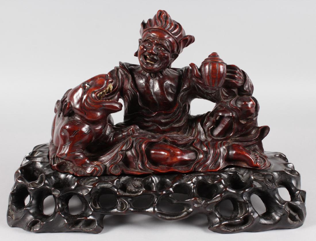 A GOOD CHINESE CARVED WOOD FIGURE of a man with a: A GOOD CHINESE CARVED WOOD FIGURE of a man with a teapot, tiger standing on a pierced stand. 16ins wide.