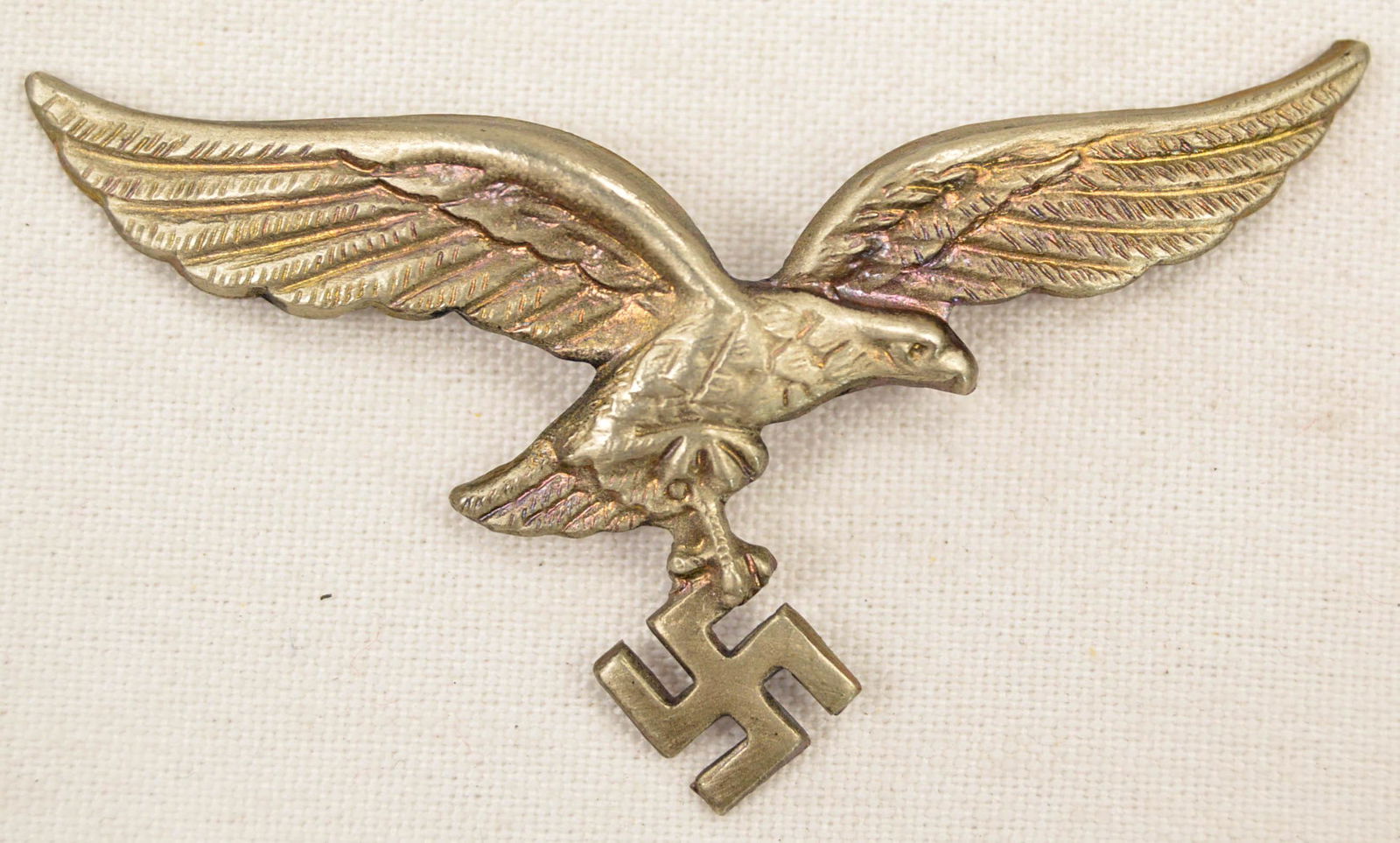 German WWII Luftwaffe NCO Visor Cap Eagle: German World War II Luftwaffe NCO Visor Cap Eagle. Measures 2 5/8” 1 1/2” tall. The front shows a Luftwaffe flying eagle clutching a swastika in his talons. Has two flat horizontal prongs on the r