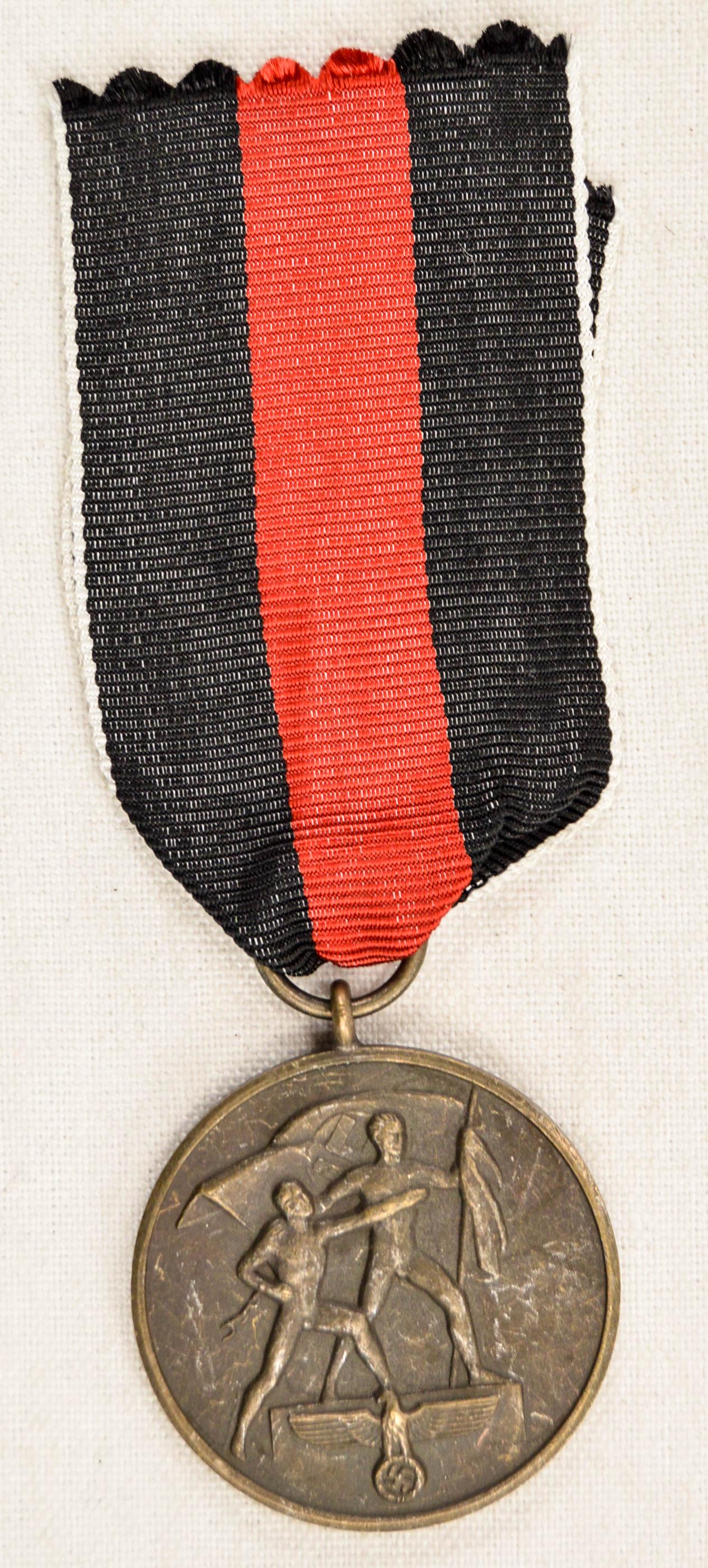 German WWII 1938 Czechoslovakian Annexation Decor: German WWII 1938 Czechoslovakian Annexation Decoration. Measures 1 1/4" in diameter. The front shows two men holding a flag with a German eagle below. The reverse side reads ‘Ein Volk – Ein Reich