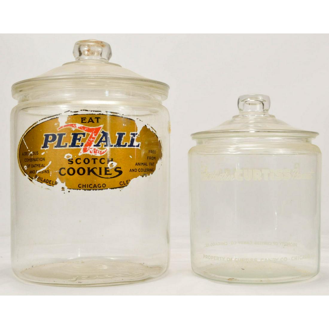 Glass Display Jars: One clear glass jar, with white writing, from Curtis Candy Co. with glass lid, in good condition and one larger glass jar, reverse label inside, Plezall scotch cookies decal in poor condition, many sc