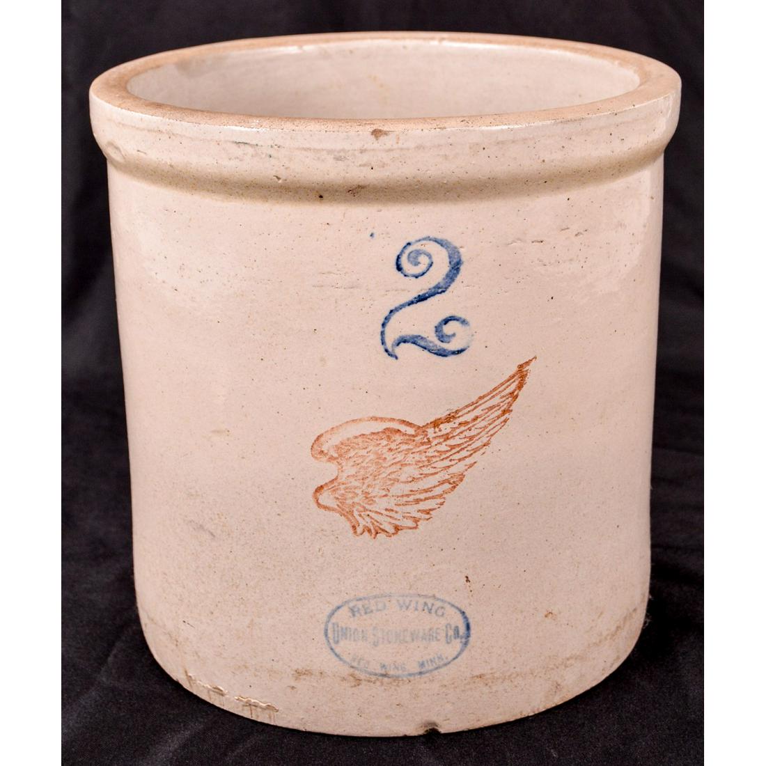 2 Gallon Red Wing Stoneware Crock: A Red Wing 2 gallon stoneware crock. Front decals are present and in very good condition with a nice red wing and blue wording. Small chip at the base and a small surface crack on the inside that does