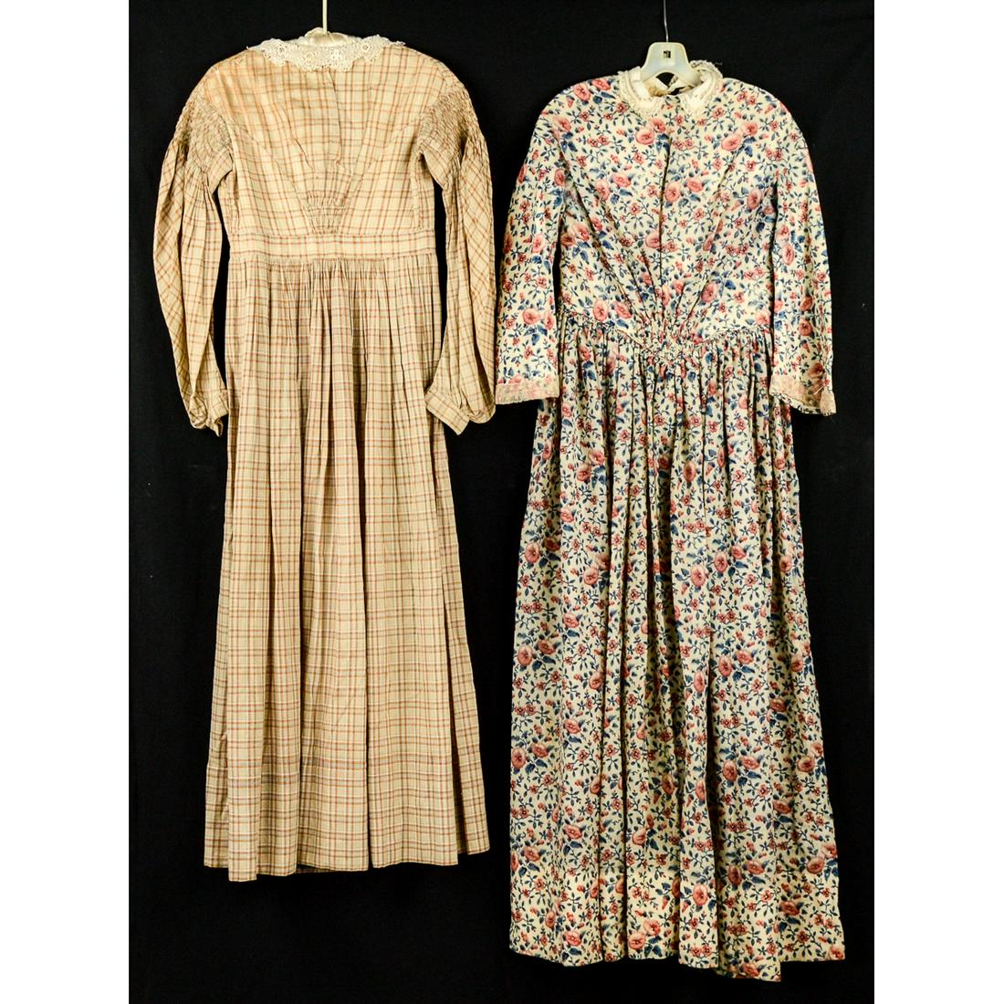 2 Ladies 1870's Prairie Dresses: Bright floral print, hook and eye closure up the back, padded bosom. 24" waist, some underarm stains and various wear throughout. Brown and tan plaid cotton prairie dress. Hook and eye closure. Lace t