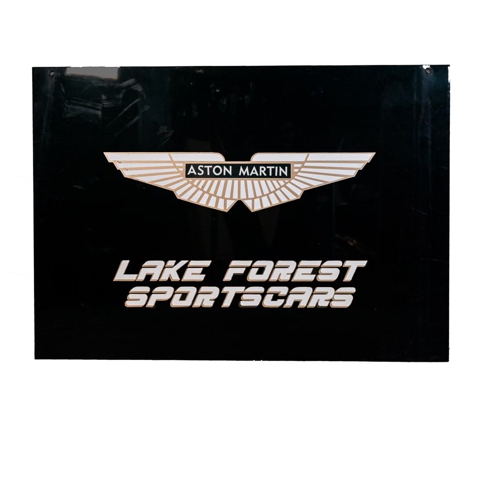 Aston Martin / Lake Forest Sportscars Sign: Two-sided Aston Martin / Lake Forest Sportscars, Ltd. dealer sign. White and gold vinyl lettering on a black metal background. Some use marks showing but overall in good condition. Ready to hang on yo