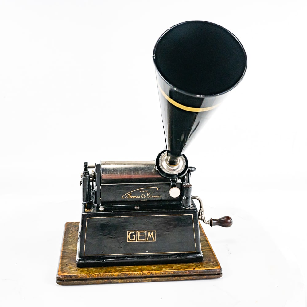 Edison Gem Model B Cylinder Phonograph: This machine with its oak cover has its original finish and banner decal both of which are showing some wear and evidence of having been lightly recoated. The top handle appears to be a replacement. T