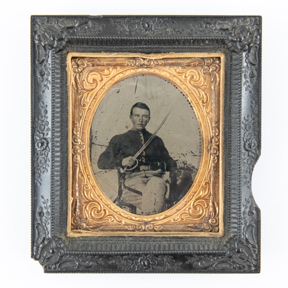 Tintype of CW Soldier With Drawn Sword: Tintype of a young seated cavalry officer in uniform holding his drawn sword in his right hand and a revolver in his left hand. Tintype is in fair condition with a horizontal crease and some image scr