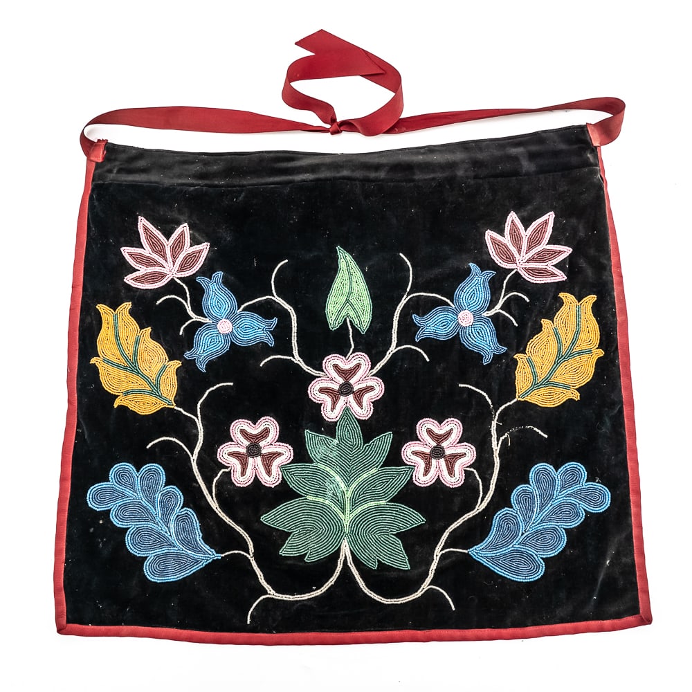 1890s Winnebago Dance Apron: Attributed as a Winnebago but possibly Chippewa or Ojibwe dance apron circa 1890s. Featuring a floral motif on a dark velvet background, trimmed in red ribbon, with red ribbon tied at the top. The bea
