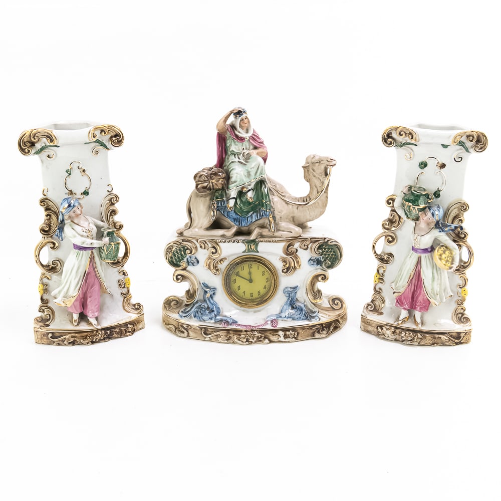 Vintage German Porcelain Bisque Clock & Vase Set: 11" porcelain figural porcelain wind up clock portraying lady riding a camel; marked Germany 6355 bottom side along with a pair of 9.5" porcelain figural vase three piece set both with marked 6354 on