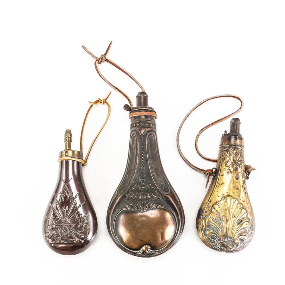 3 Vintage Brass & Copper Gunpowder Flasks: Collection features three distinctive black powder flasks, essential gear for the 19th-century marksman. The largest is a classic copper-bodied flask featuring a double-sided embossed design, clearly