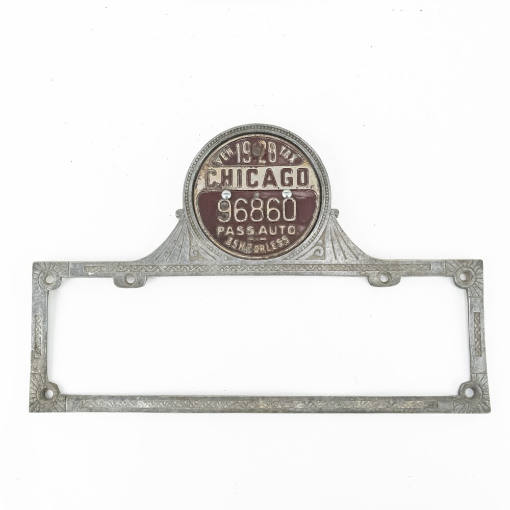 1930's Aluminum License Plate & Tag Frame: Nice cast aluminum Art Deco style frame made to fit 13.5" wide X 4.5" tall plates and 4" diameter city tags. In VG original condition. Comes with a 1928 Chicago tag. See pics. From the Jim Dvorak coll