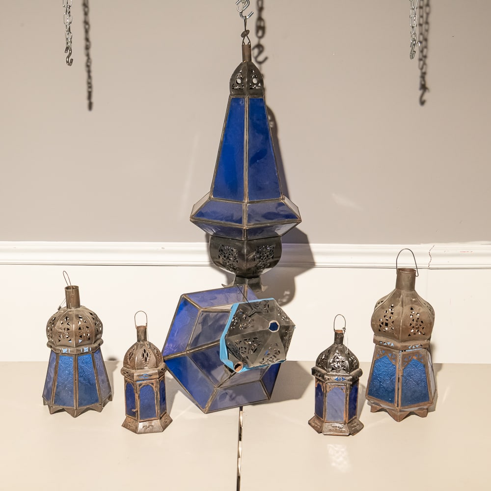 Six Moroccan Style Blue Glass Lanterns (6): This striking collection of six Moroccan-style "Henn" lanterns showcases the classic fusion of intricate metalwork and vibrant cobalt blue glass. Each piece features traditional pierced "Moucharaby"