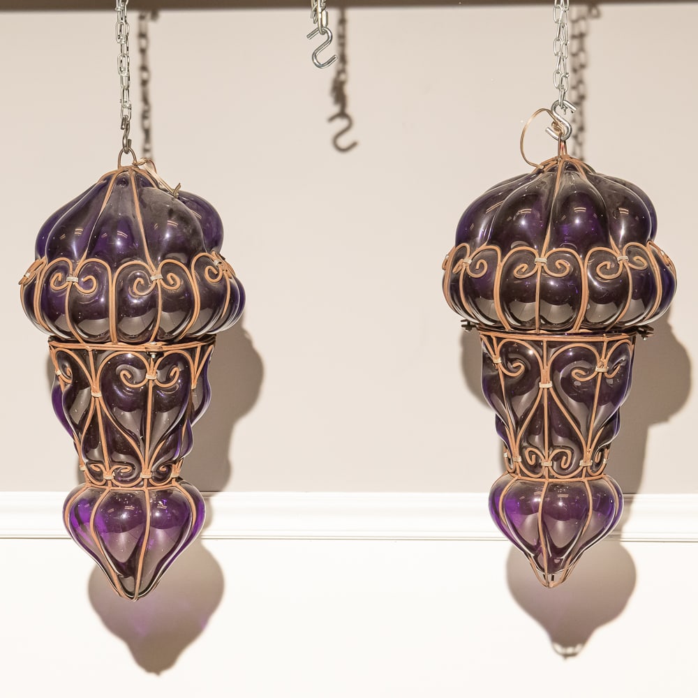 Large Purple Blown Glass Lanterns (2) W/Rods(2): These striking Moroccan-style "onion" lanterns feature deep amethyst hand-blown glass encased in intricate, scrolled iron wire cages. The vibrant purple hue and the bulbous, multi-tiered form suggest