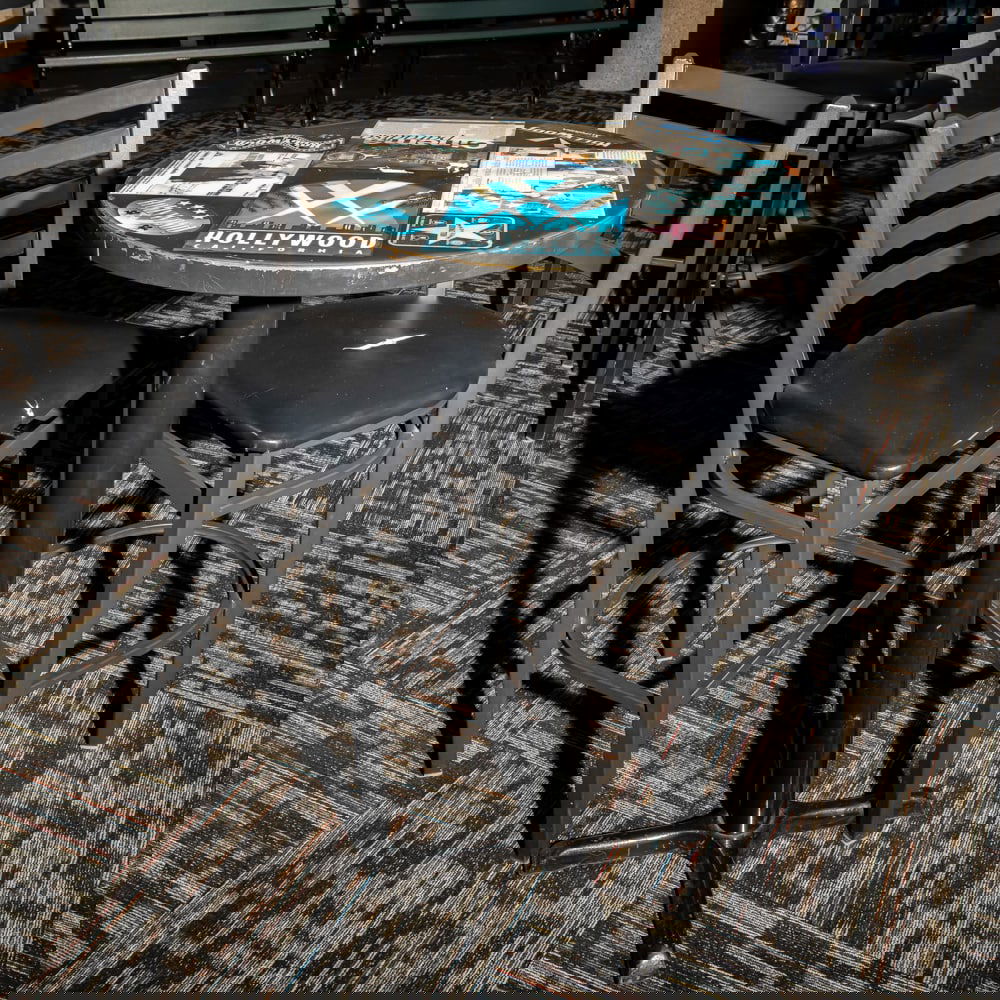Cinema-Themed Bistro Table w/2 Chairs: This eye-catching bistro set features a round pedestal table topped with a collage of Hollywood-themed graphics, including classic cinema advertisements and "Hollywood" signage, capturing a mid-to-lat