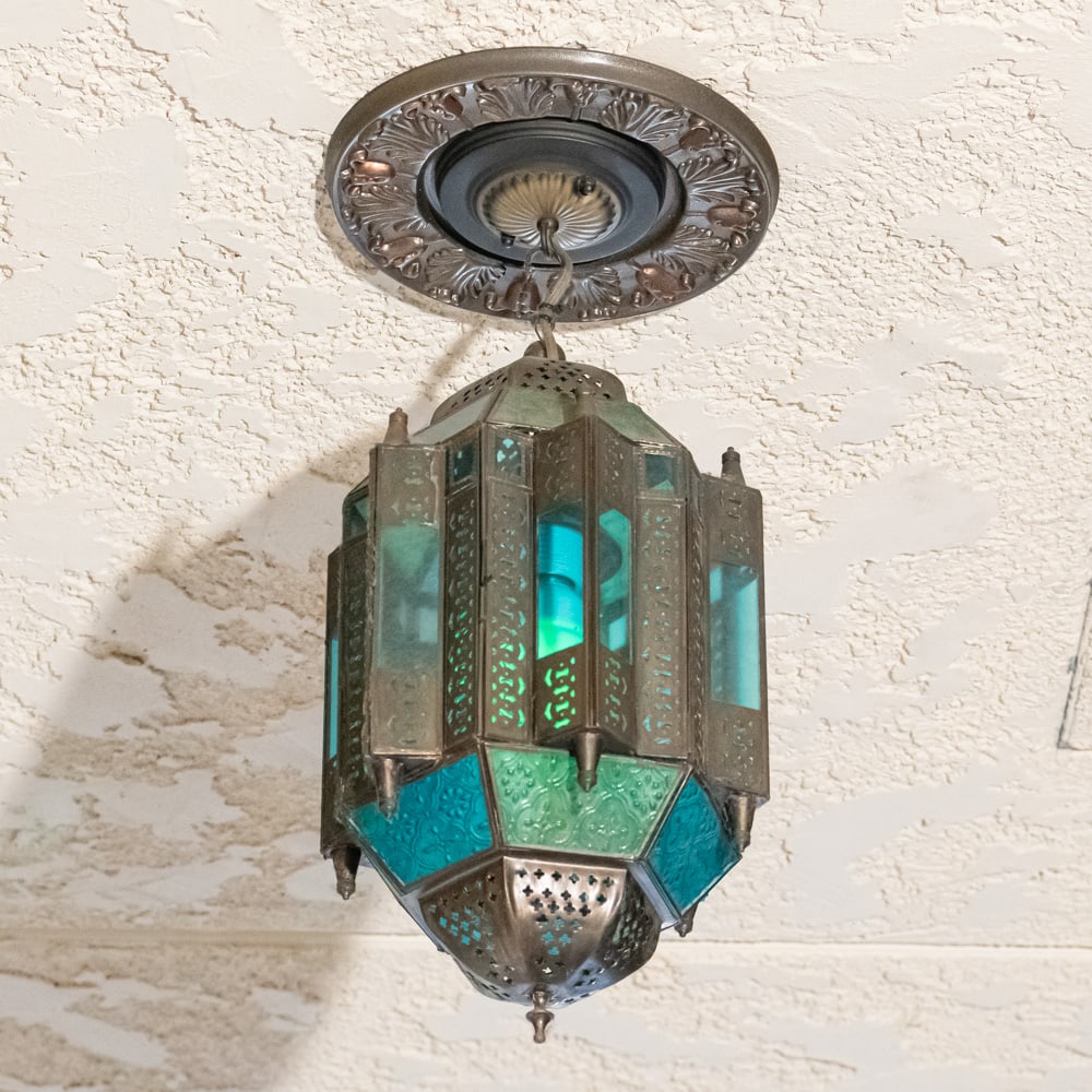 Vintage Moroccan Style Stain Glass Chandelier Exit: This Moroccan-inspired hanging chandelier captures the essence of Moorish design with its intricate pierced metalwork and vibrant stained glass panels in shades of emerald green and turquoise blue.