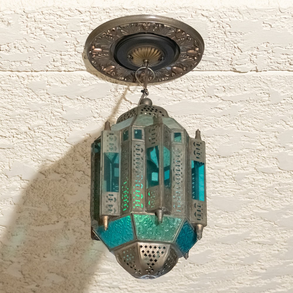 Vintage Moroccan Style Stain Glass Chandelier Exit: This Moroccan-inspired hanging chandelier captures the essence of Moorish design with its intricate pierced metalwork and vibrant stained glass panels in shades of emerald green and turquoise blue.