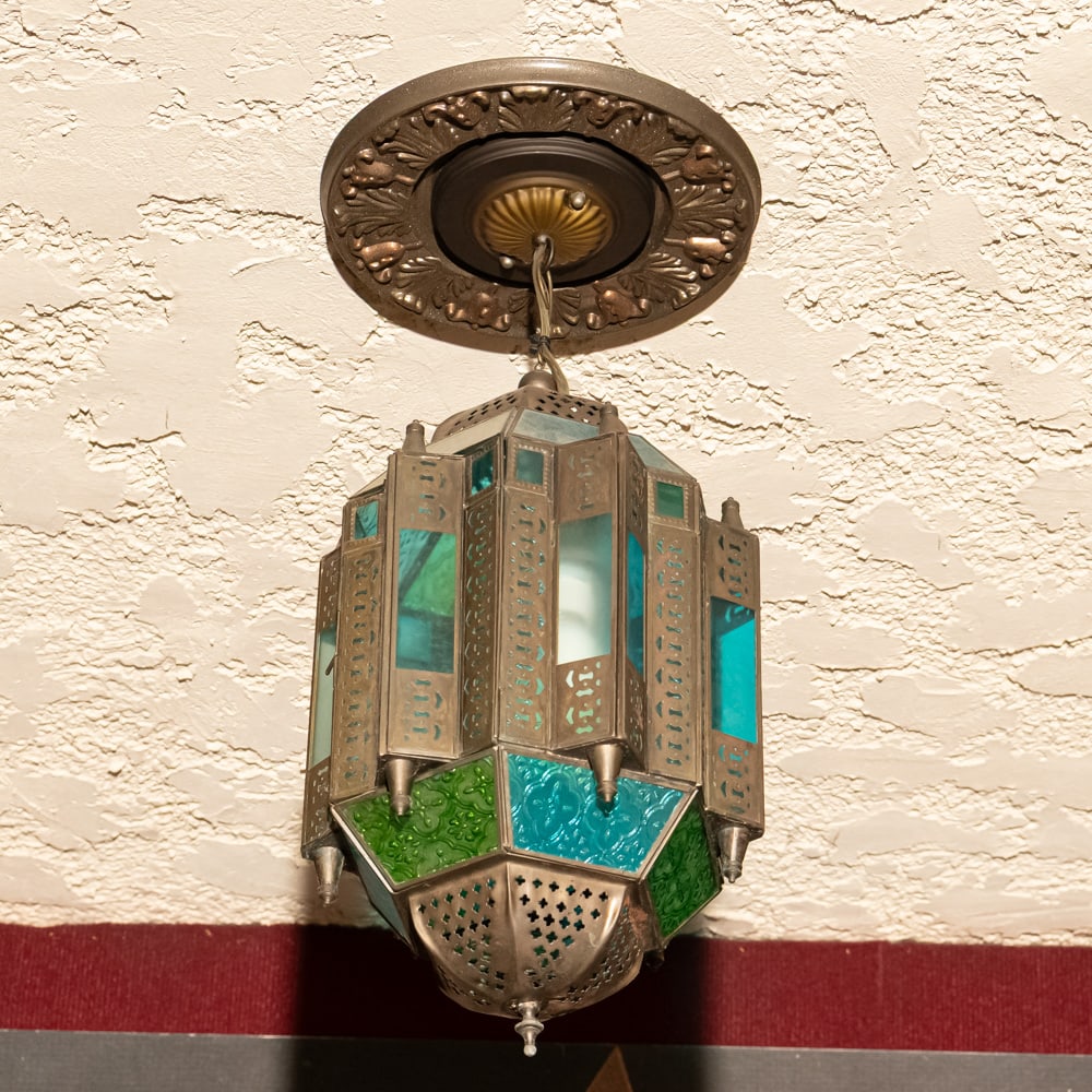 Vintage Moroccan Style Stain Glass Chandelier Exit: This Moroccan-inspired hanging chandelier captures the essence of Moorish design with its intricate pierced metalwork and vibrant stained glass panels in shades of emerald green and turquoise blue. Th