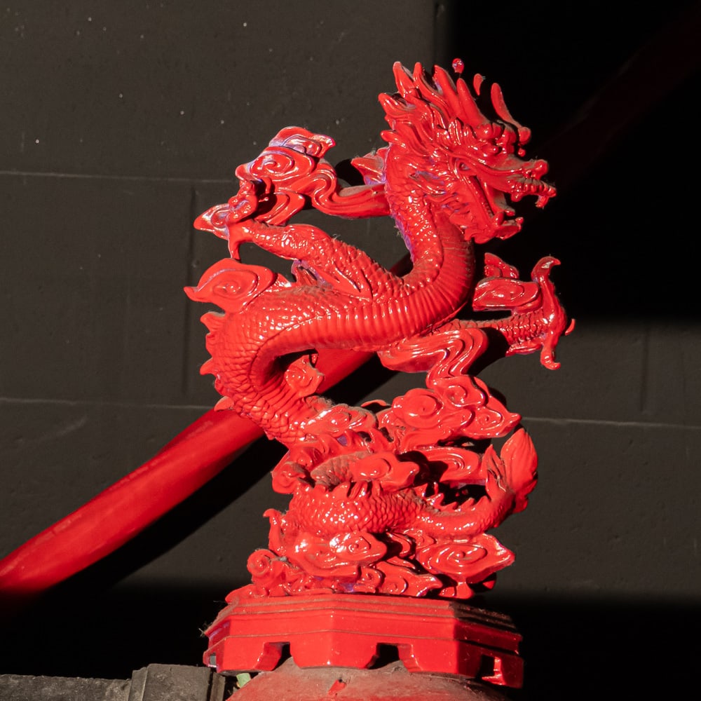 Red Dragon Top Corner: Carved Cinnabar Style Red Dragon StatueThis striking piece captures the power and fluid motion of a classic Chinese Imperial dragon, intricately detailed with deep-relief carvings that mimic the tradi