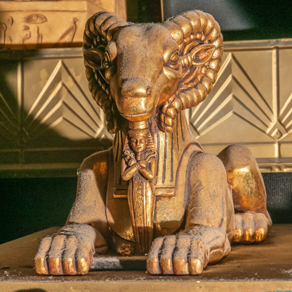 Sphinx-like Ram Carved Statue Left: Majestic recumbent ram statue featuring large eye catching carved horns. Ram lies in sphinx like divine protective pose with hind legs extended while the front ones are folded. This is the right side