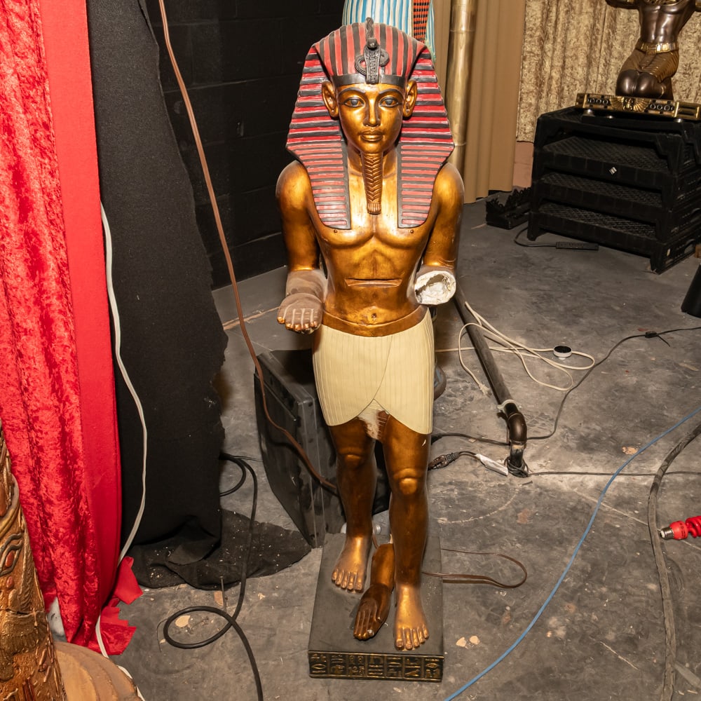 Pharaoh Statue w/Broken Arm: Gilded King Tut Egyptian StatueThis striking floor statue captures the iconic likeness of King Tutankhamun in a traditional Egyptian Revival style. Crafted from a molded composite or fiberglass materi