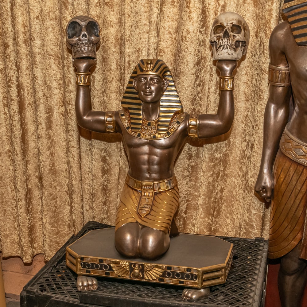 Kneeling Pharaoh Statue Left: Striking composite resin statue captures a kneeling Egyptian pharaoh in a ceremonial pose, rendered with a faux-bronze finish and accented by traditional gold-tone "nemes" headcloth striping. The