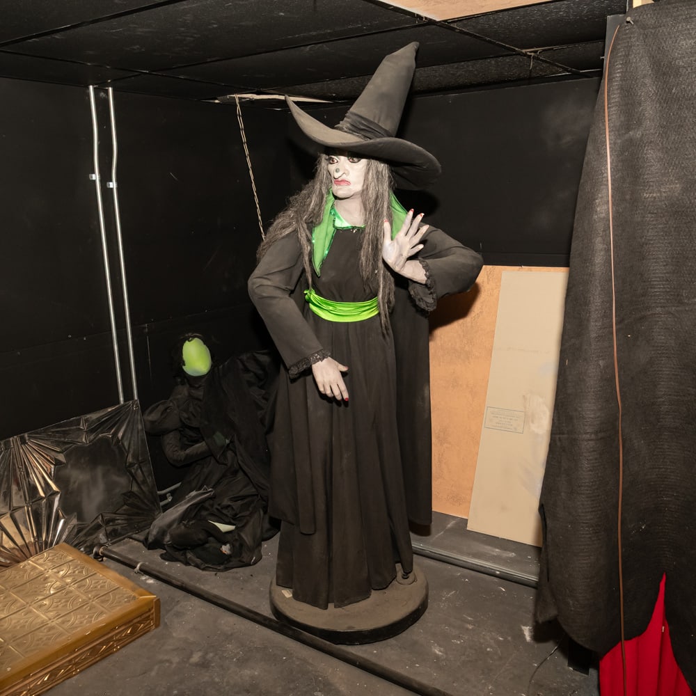 Life-Size Animated Wicked Witch Prop: This classic life-size anima-tronic depicts a wicked witch in the traditional style, featuring a pointed "crumpled" hat, tattered black robes, and a vibrant lime green sash and collar that pop