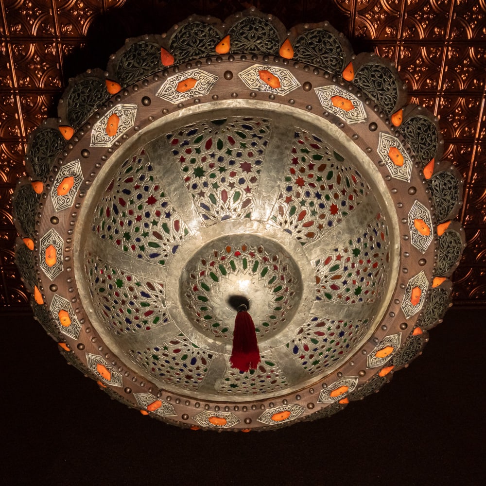 Moroccan Pierced Brass & Stained Glass Lamp: This exquisite Moroccan-style ceiling fixture is a masterclass in Moorish craftsmanship, likely dating from the mid-to-late 20th century. The piece features intricate, hand-pierced brass filigree that