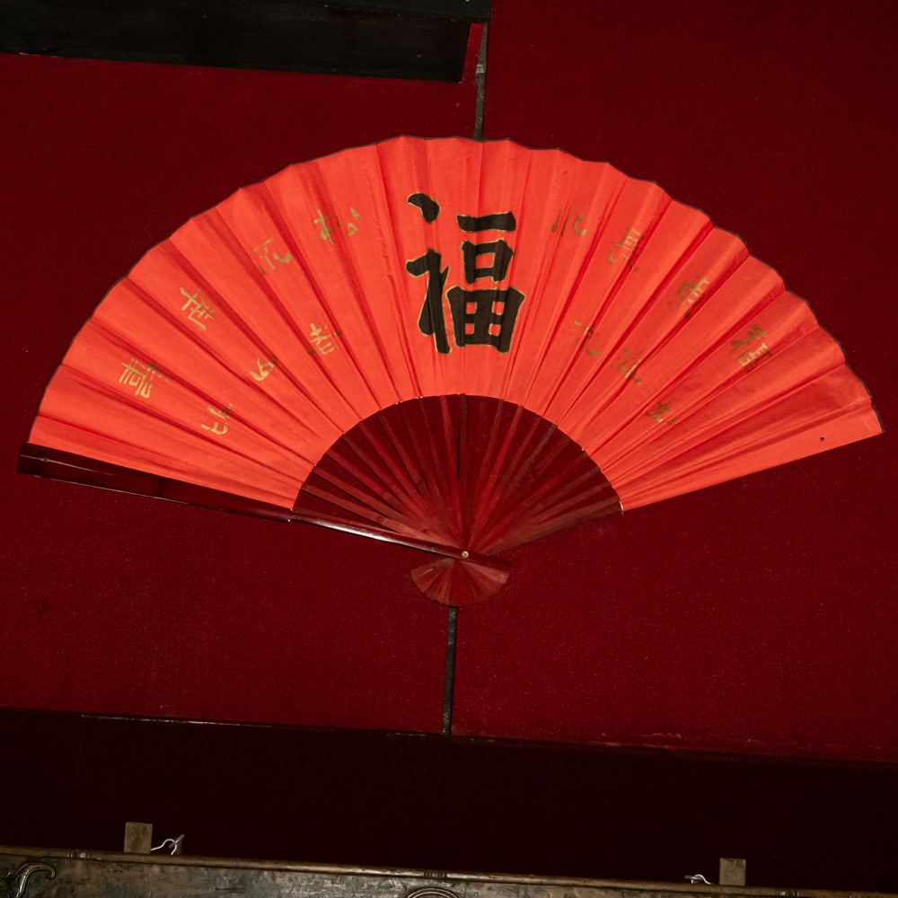 Large Vintage Red Chinese "Fu" Wall Fan (L): This is an impressive, oversized decorative folding wall fan featuring a vibrant red paper or fabric leaf. The central focal point is a large, hand-painted black calligraphy character for "Fu", repres