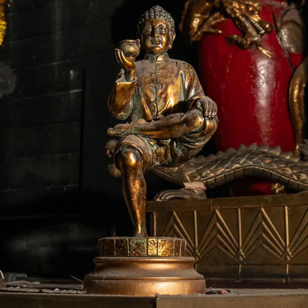 Gilded Seated Buddha Statue: A striking piece of Orientalist decor, this statue depicts a seated Buddha-like figure in a unique, dynamic pose, balancing on one leg while holding a small vessel or offering bowl. The figure is dres