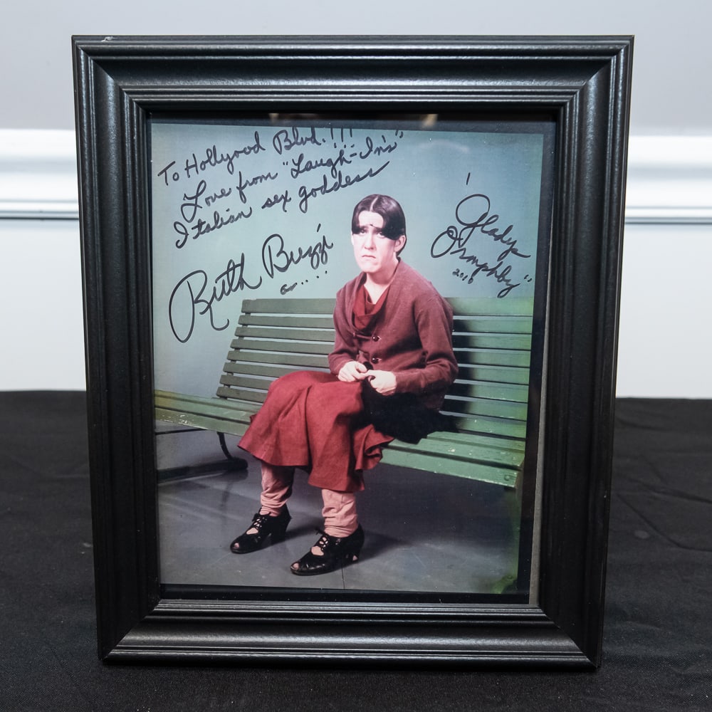 Framed Signed Ruth Buzzi Gladys Ormsby 8x10: This is a fantastic piece of television history featuring the legendary Ruth Buzzi in her iconic role as the spinster Gladys Ormsby from "Rowan & Martin's Laugh-In." The photo is personalized to "Holl