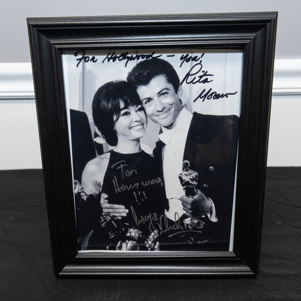 Framed Rita Moreno & George Chakiris Signed 8x10: This is a captivating piece of Hollywood history featuring a black and white photograph of Rita Moreno and George Chakiris posing with their Academy Awards for the 1961 film West Side Story. Both acto