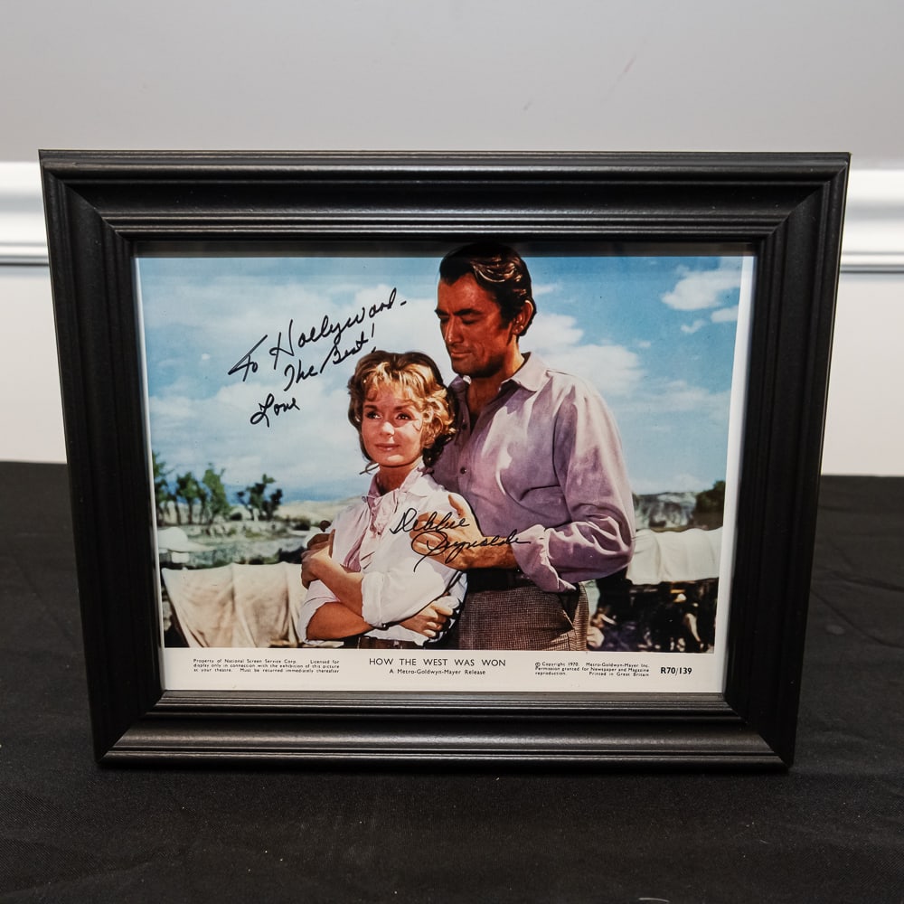 Framed Debbie Reynolds Signed Movie Still 8x10: This is a wonderful piece of Hollywood history: an original promotional movie still from the 1962 epic How the West Was Won, featuring a vibrant signature from the legendary Debbie Reynolds. The "Metr