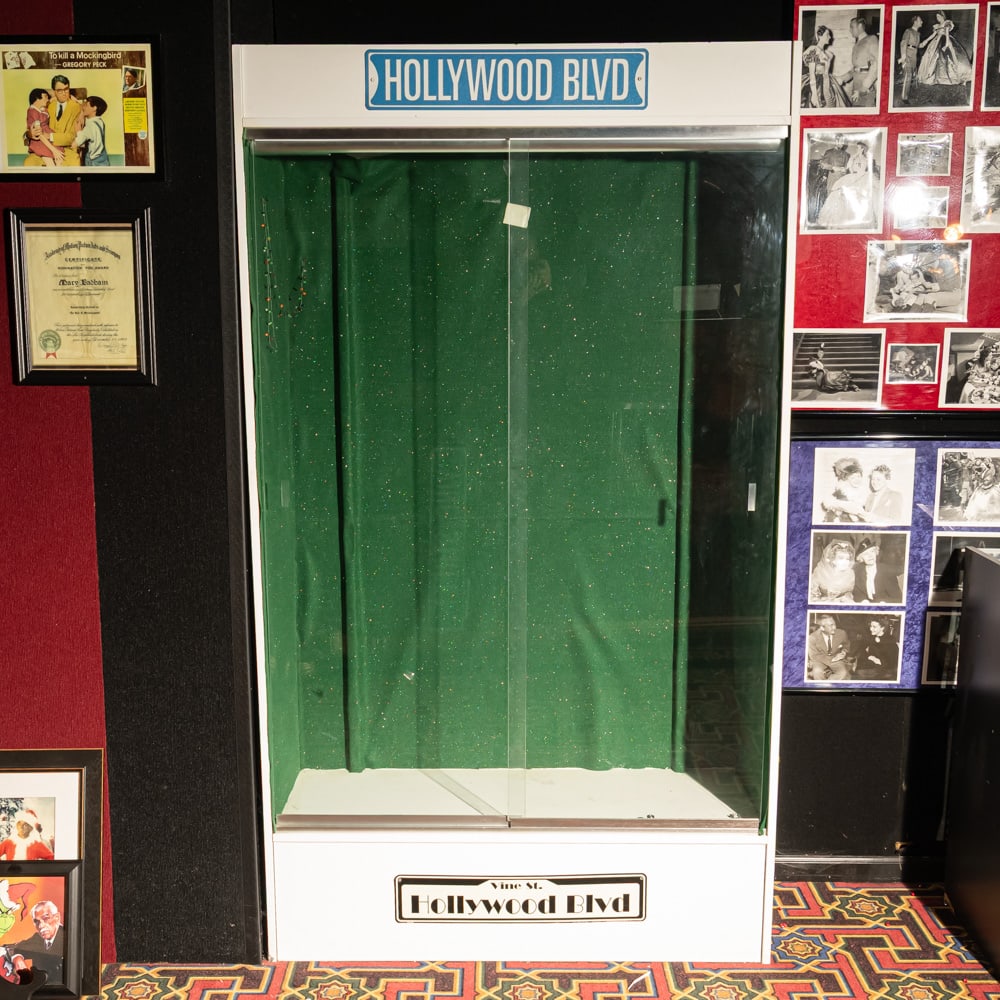 Museum Display Case: Museum display case for showcasing high-end props or costumes. This modern, towering cabinet features a clean white laminate finish, accented by iconic blue and white "Hollywood Blvd" and "Vine St" st