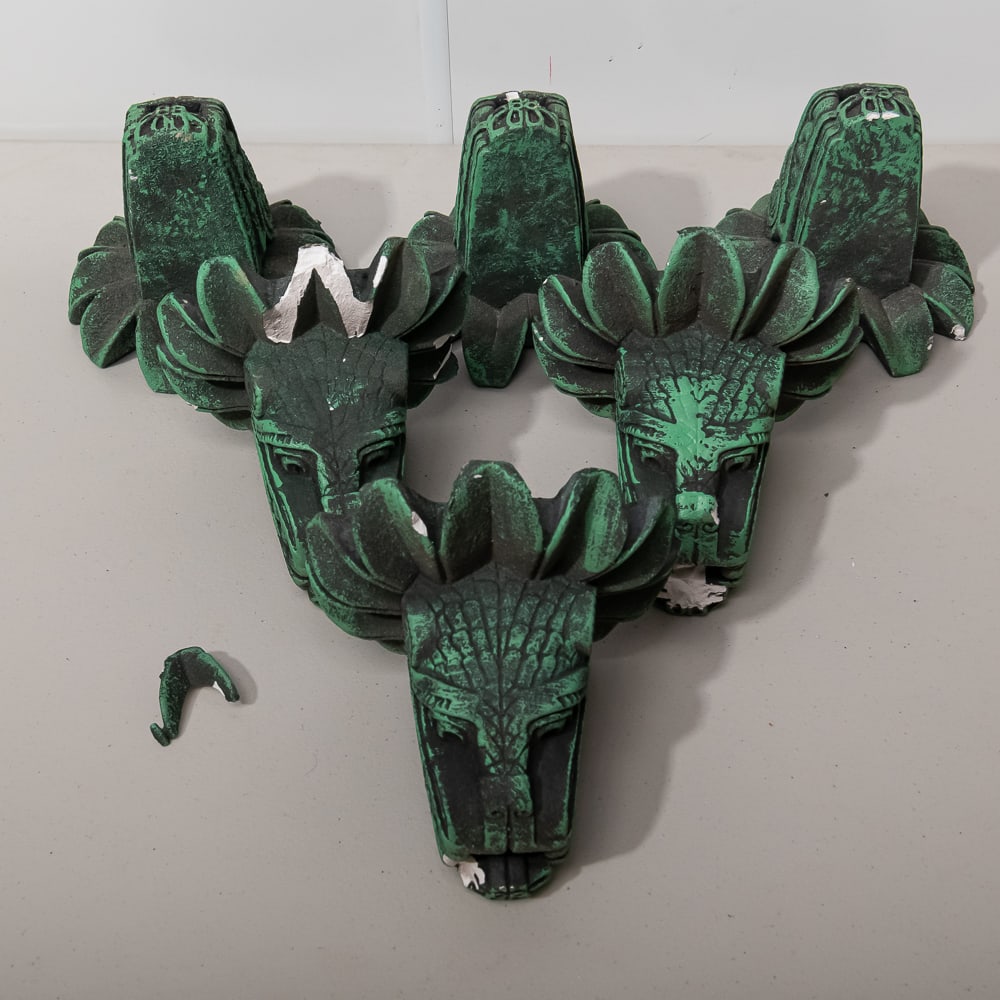 Six Verdigris Finish Plaster Dragon Heads (6): This collection of six cast plaster dragon heads features a striking Mesoamerican-inspired aesthetic, reminiscent of the feathered serpent deity Quetzalcoatl. Each piece is finished in a weathered bla