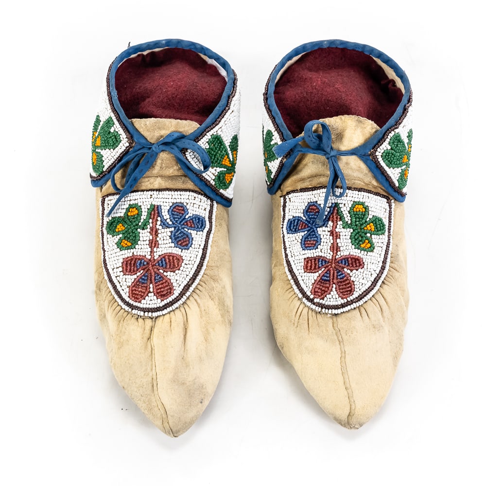 Beaded Native American Moccasins: This exceptional pair of Native American style moccasins features beautifully executed, tight beadwork showcasing vibrant floral and clover motifs against a solid white beaded ground on both the