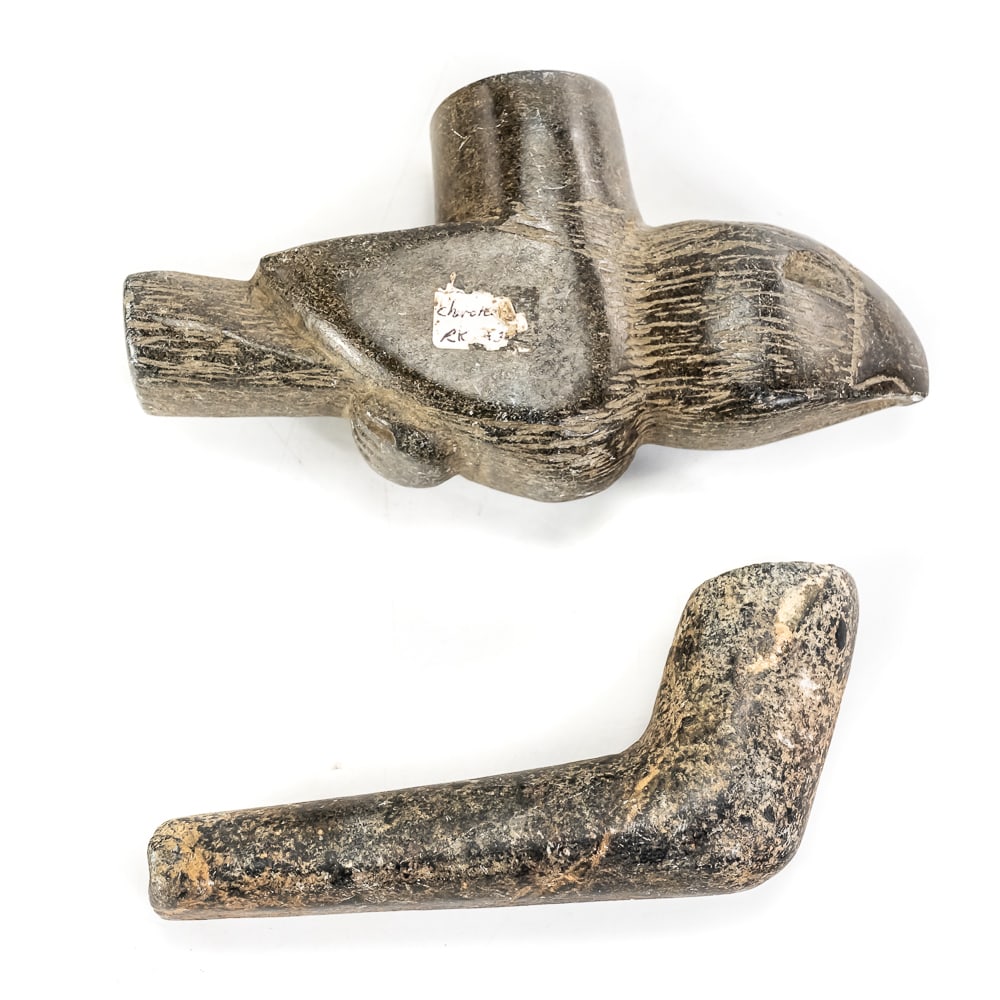 Native American Style Carved Stone Pipes: Two carved stone smoking pipes. The first is a classic, plain L-shaped elbow pipe featuring a mottled dark grey and brown stone composition with subtle lighter speckling. The second is an effigy pipe