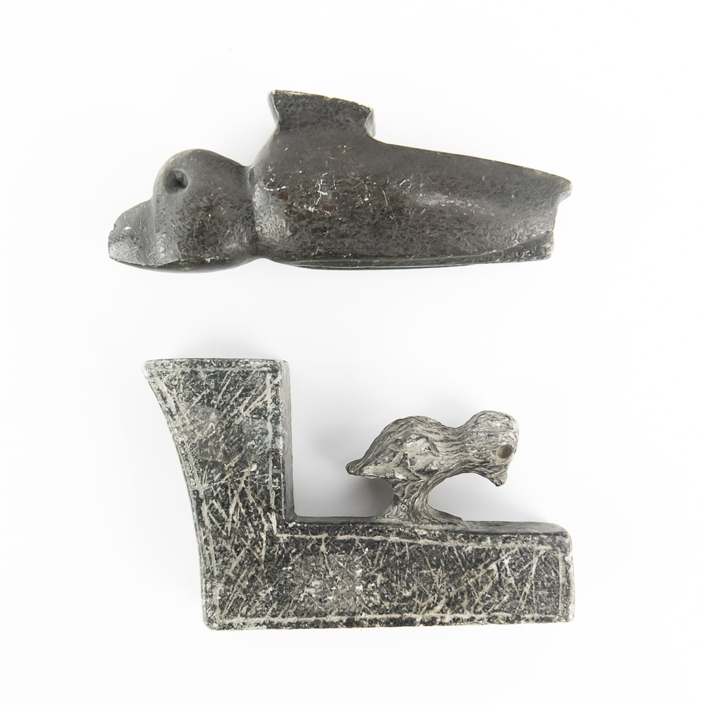 Two Native American Style Stone Effigy Pipes: This lot features two Native American style stone effigy pipes carved from dark, dense stone. The first is a sleek zoomorphic pipe featuring a stylized bird or animal head carving at the bowl end,