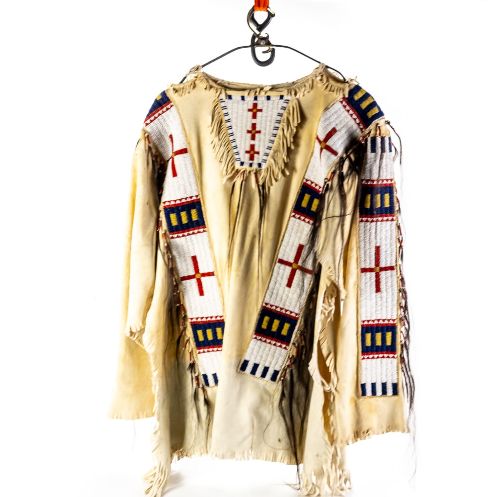 Plains-Style Beaded Buckskin War Shirt: This striking Plains-style hide war shirt features elaborate hand-stitched seed beadwork in a traditional geometric palette of white, red, yellow, and deep blue. The garment is constructed from soft-t
