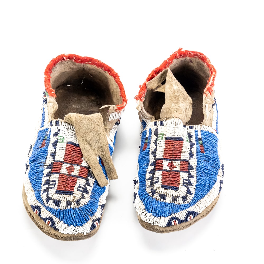 Plains Indian Style Beaded Moccasins Pair: These late 19th to early 20th-century style Plains Indian moccasins showcase exceptional craftsmanship, featuring dense "lazy stitch" beadwork on brain-tanned hide. The vibrant geometric motifs,