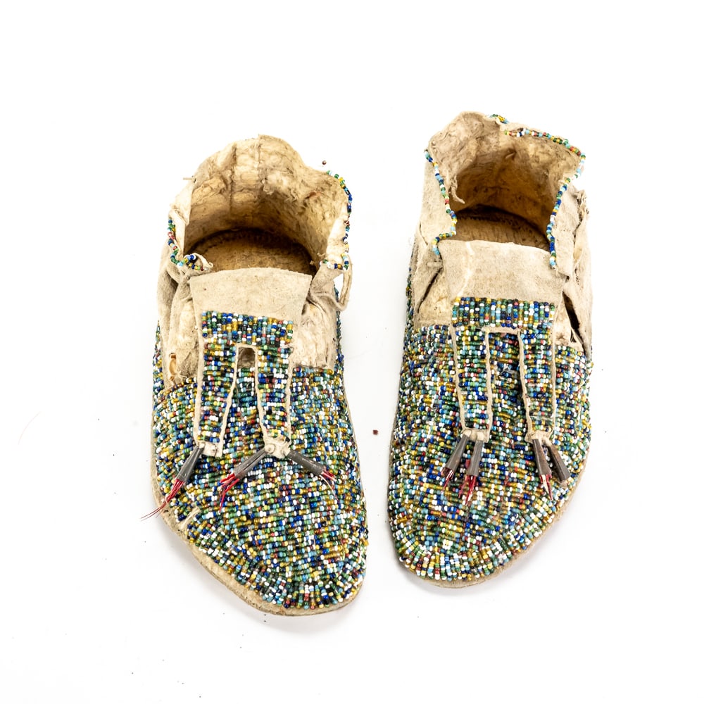 Antique Fully Beaded Plains Moccasins Pair: These striking Plains Indian style moccasins showcase remarkable craftsmanship, featuring a fully beaded "lazy stitch" design with a vibrant palette of translucent and opaque seed beads. Constructed