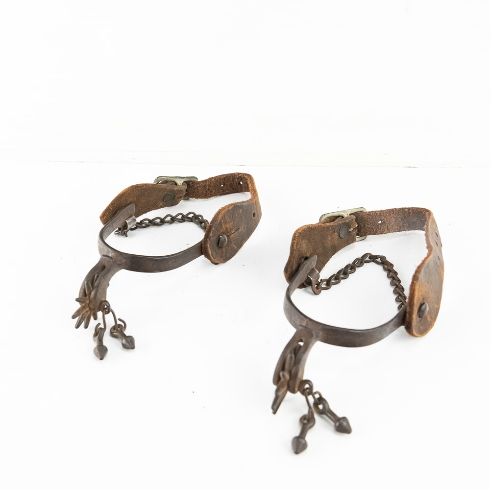 Vintage Iron Cowboy Spurs Same-Side Pair: These are a rugged pair of vintage forged iron cowboy spurs, notable for being a matching "same-side" set rather than a mirrored pair. Both spurs feature the same orientation on the iron heel bands