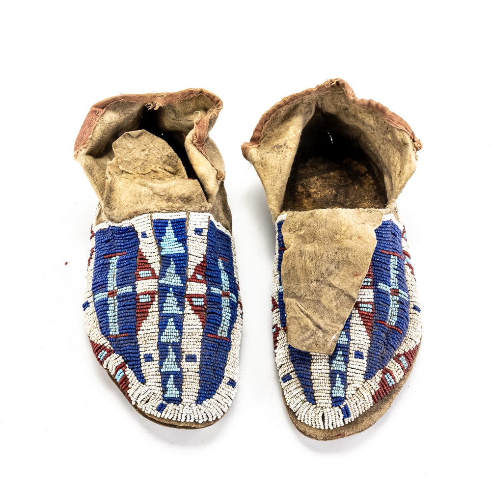 Plateau Beaded Hard-Sole Moccasins Pair: These striking Native American Plateau-style moccasins feature vibrant, full-coverage seed beadwork in a traditional geometric pattern. The design utilizes a palette of deep cobalt blue, white, and