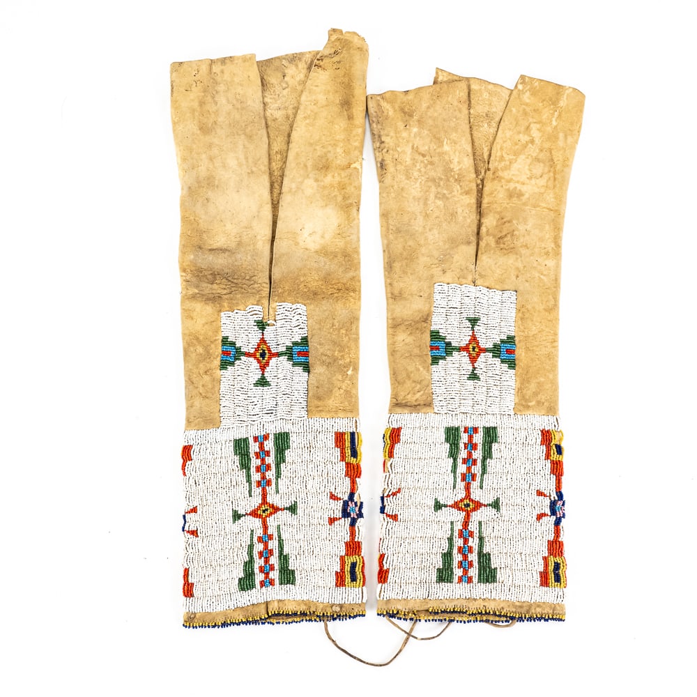Native American Beaded Hide Leggings Pair: These Plains-style hide leggings feature traditional geometric beadwork on brain-tanned buckskin, showcasing vibrant lazy-stitch patterns with cruciform and stepped-triangle motifs in white, red,