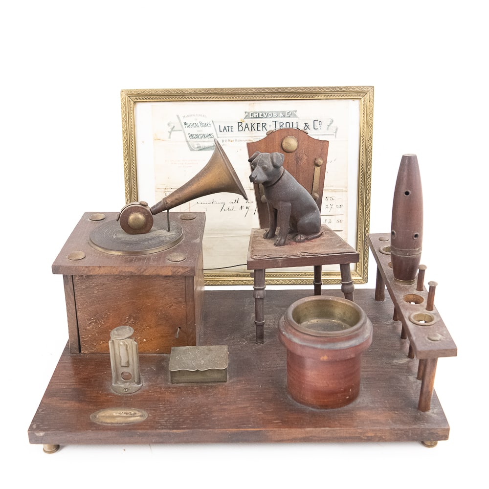 1907 His Master's Voice Smoking Set Music Box: A wood and metal smoking set depicting a stylized version of the dog looking into the phonograph horn, "His Master's Voice". The box of the phonograph contains a small mechanical music box that is wou