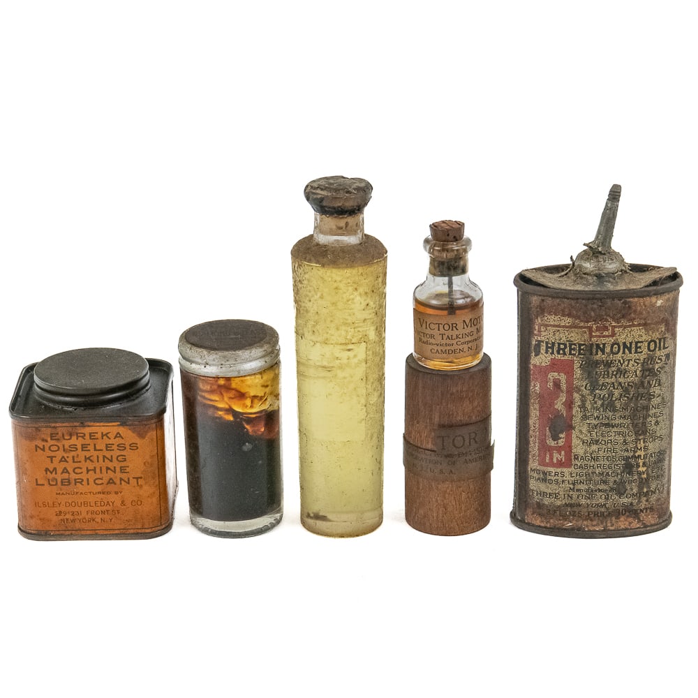 5 Piece Lot of Various Phonograph Lubricants: Consists of one large Edison grease bottle, one Eureka talking machine lubricant can, one unmarked glass bottle with oil, one Victor motor oil bottle in its original two-piece round wooden container