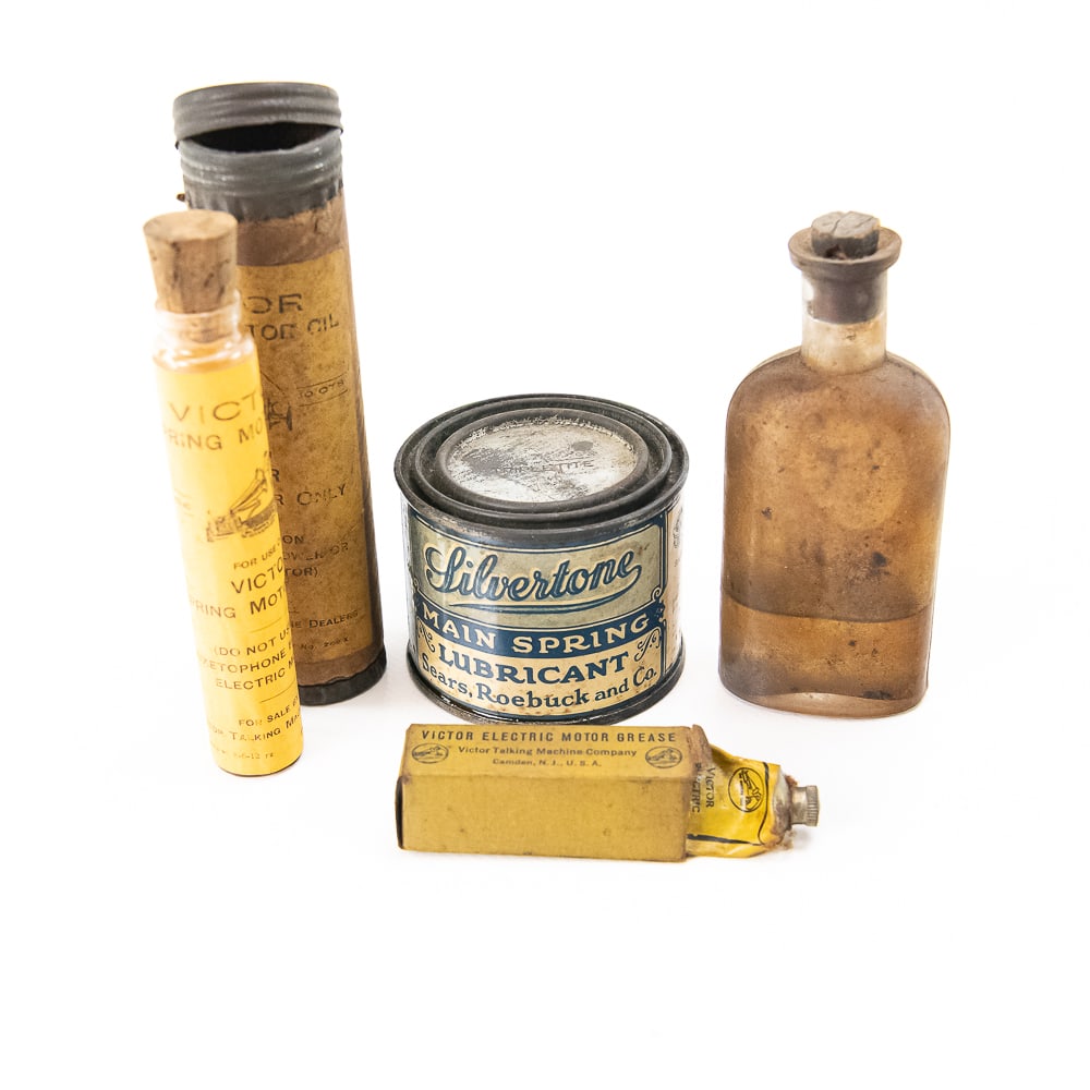 4 Piece Lot of Various Phonograph Oils and Lubes: Includes one Victor original oil bottle in its original cardboard tube, one Victor electric motor grease in its original cardboard box missing its lid, one can of Silvertone main spring grease