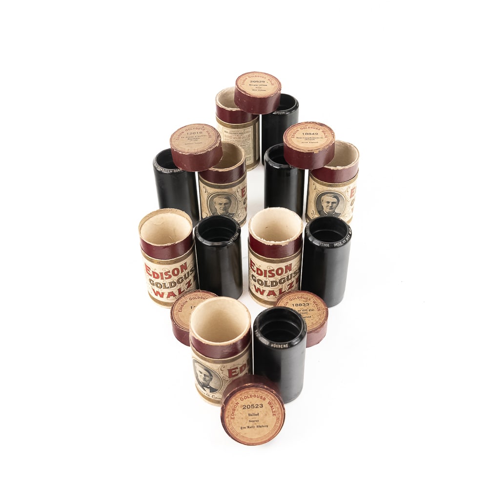 Six Edison Goldguss Cylinder Records: This lot features six individual dark wax composition cylinders produced by Thomas A. Edison's firm for the European market, each paired with its original cardboard storage tube featuring the lithogra