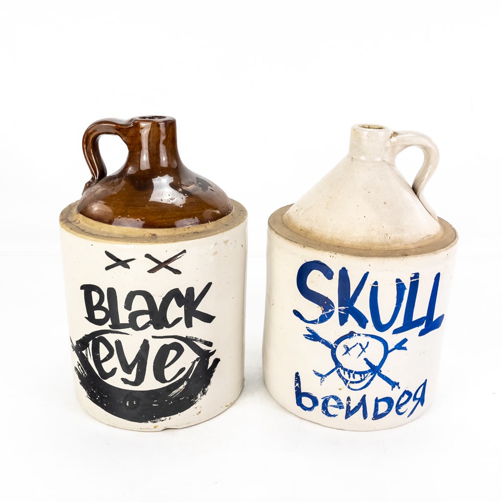 (2) Vintage Monmouth Pottery Stoneware Jugs: (2) Vintage Monmouth Pottery Stoneware Jugs, decorated with custom paint "Black Eye" and "Skull Bender", moonshine whiskey jug, two-tone brown top and tan base, age-related wear, some chips, no