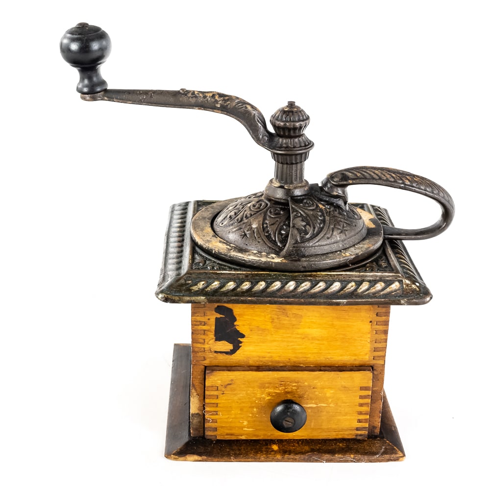 Antique Box-Style Manual Coffee Grinder: Antique Box-Style Manual Coffee Grinder, featuring an ornate cast iron hopper assembly, embossed top plate with a swivel door for loading coffee beans, long curved handle connects directly to an inter